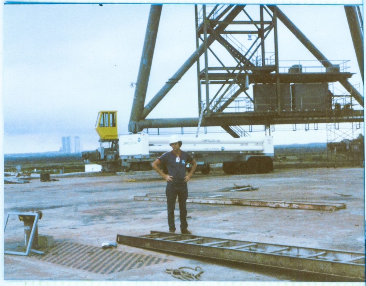 The newly-constructed Rotating Service Structure at Space Shuttle Launch Complex 39-B, Kennedy Space Center, Florida, has had its temporary supporting falsework removed from beneath it, and now stands fully self-supporting, bearing its own loads. James MacLaren stands underneath it, and in this view, you can see the heavy steel of Column Line 7 behind him and the VAB in the far distance, beyond that.